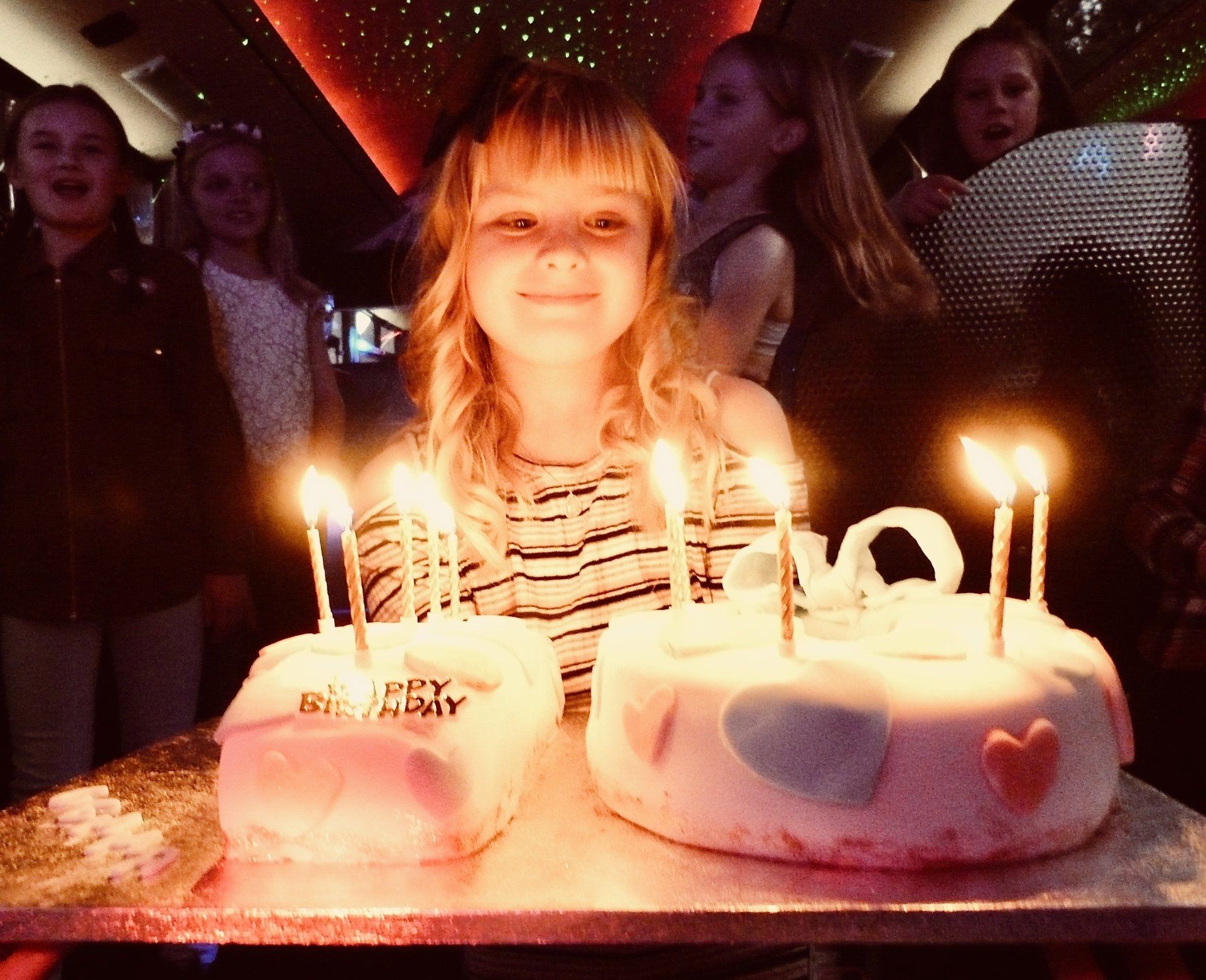 A little girl stands in front of two birthday cakes