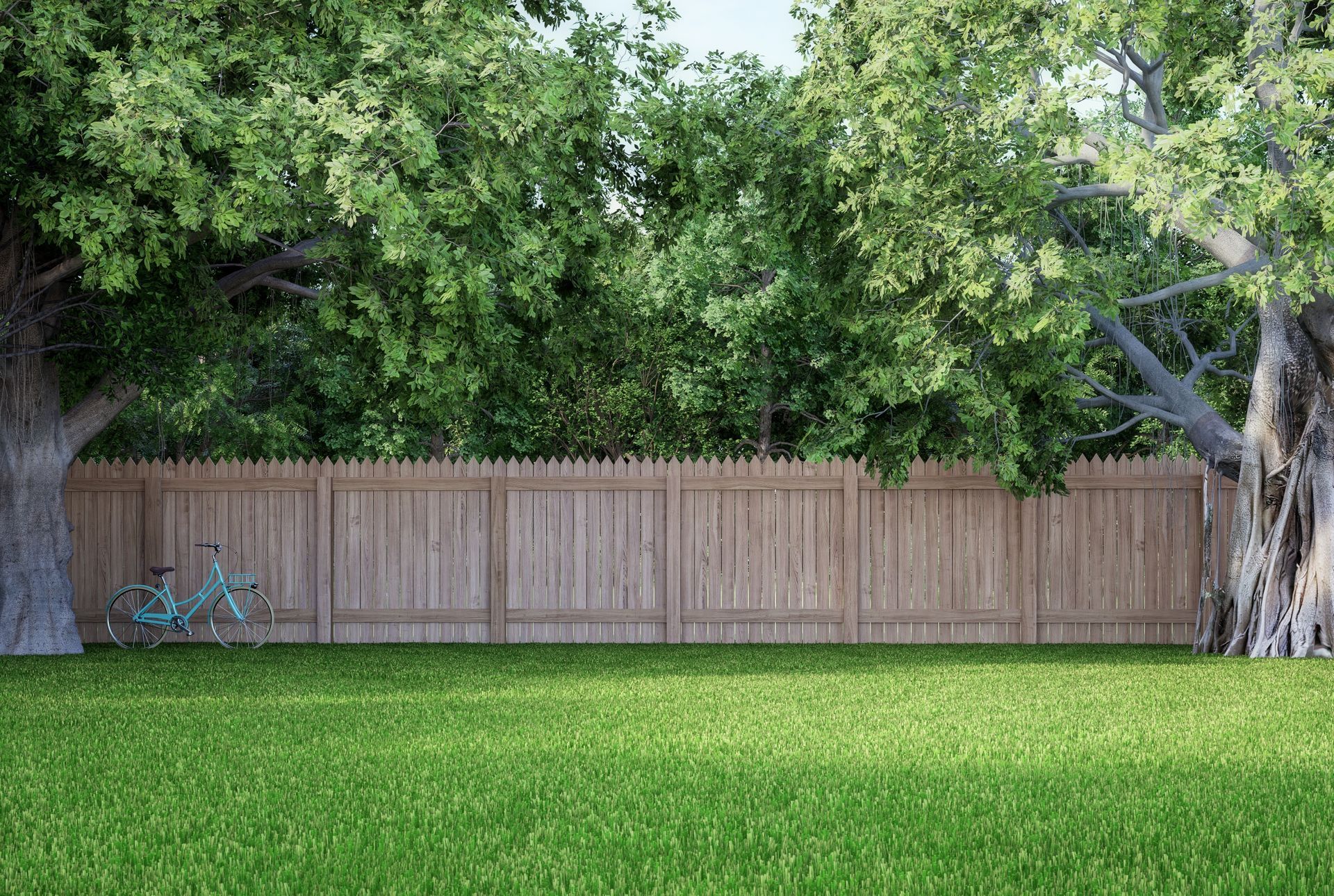 A wooden fence surrounds a lush green lawn with trees in the background.