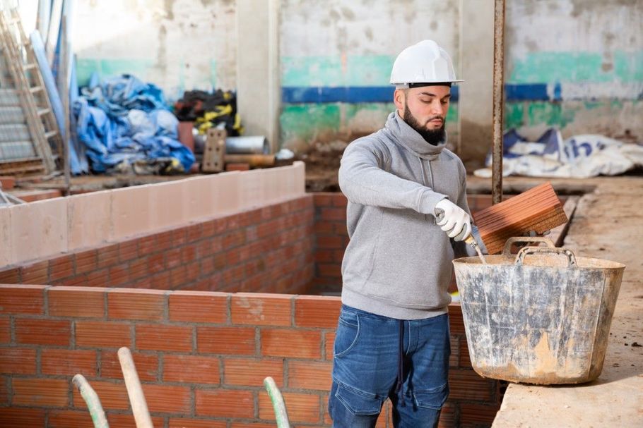 Worker in hard hat and gloves spreading mortar on a brick wall at a construction site