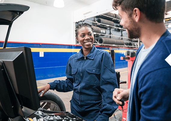 A man and a woman are working on a car in a garage.