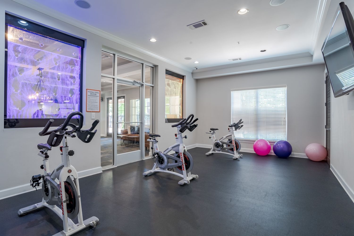 Gym with spin bikes, exercise balls, and a view into another room.