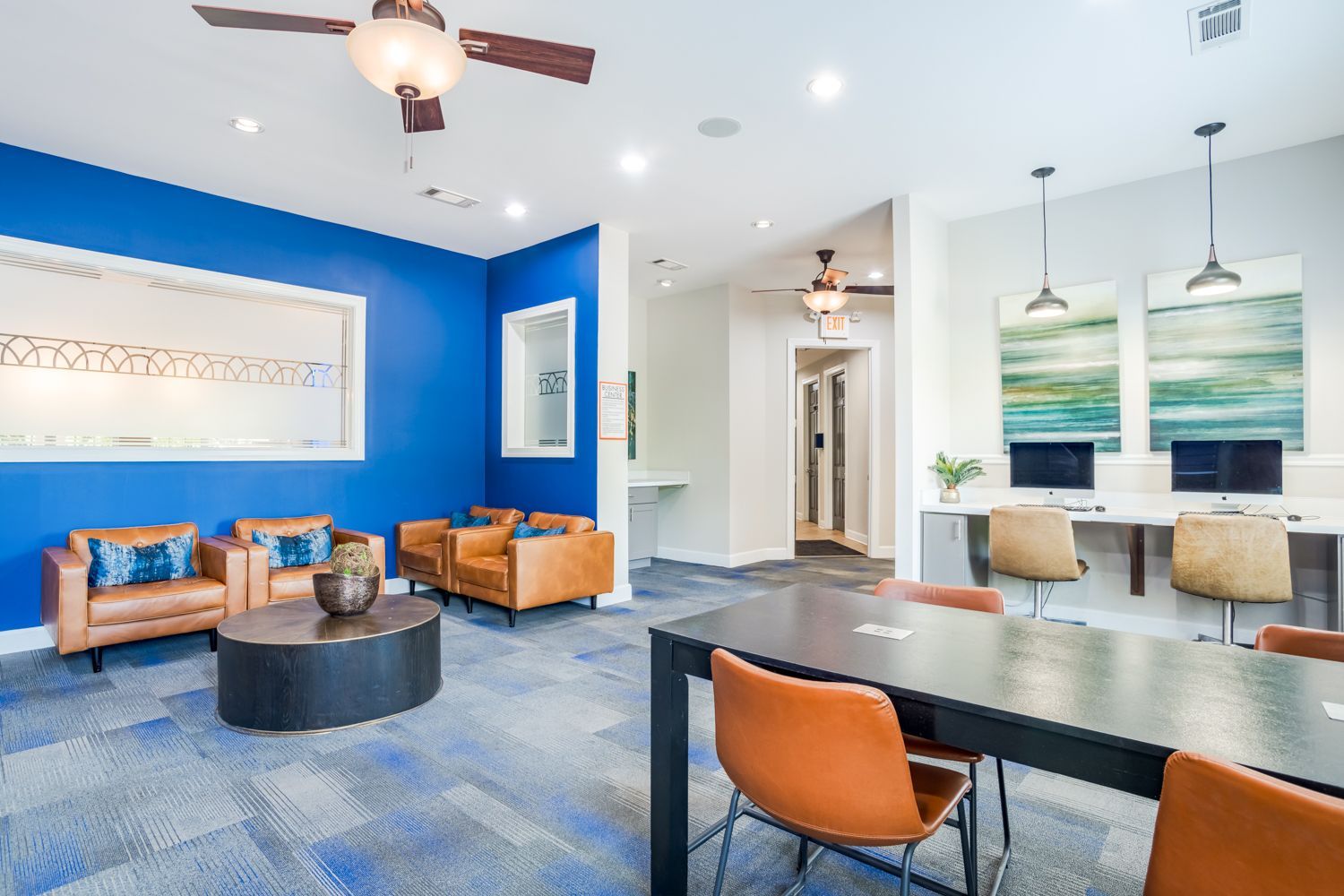 Lounge area with blue walls, brown leather chairs, a round coffee table, and a black table with orange chairs.