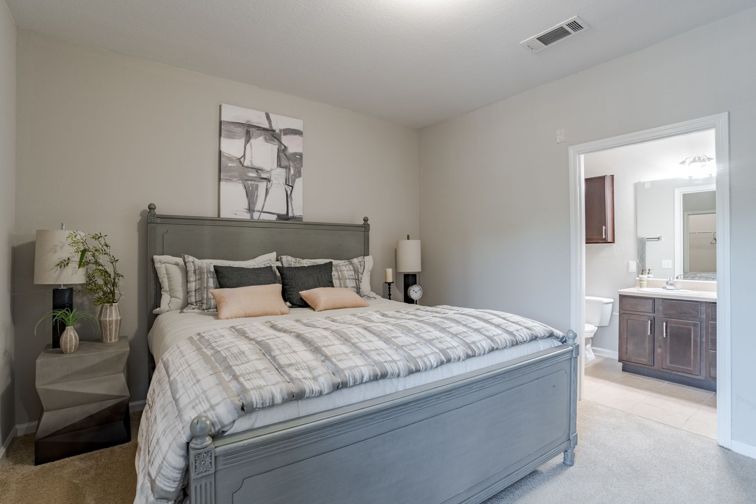 Bedroom with gray bed, nightstands, and artwork; bathroom visible through doorway.