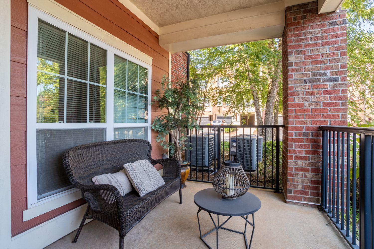 Balcony with wicker furniture, brick pillar, and view of trees.