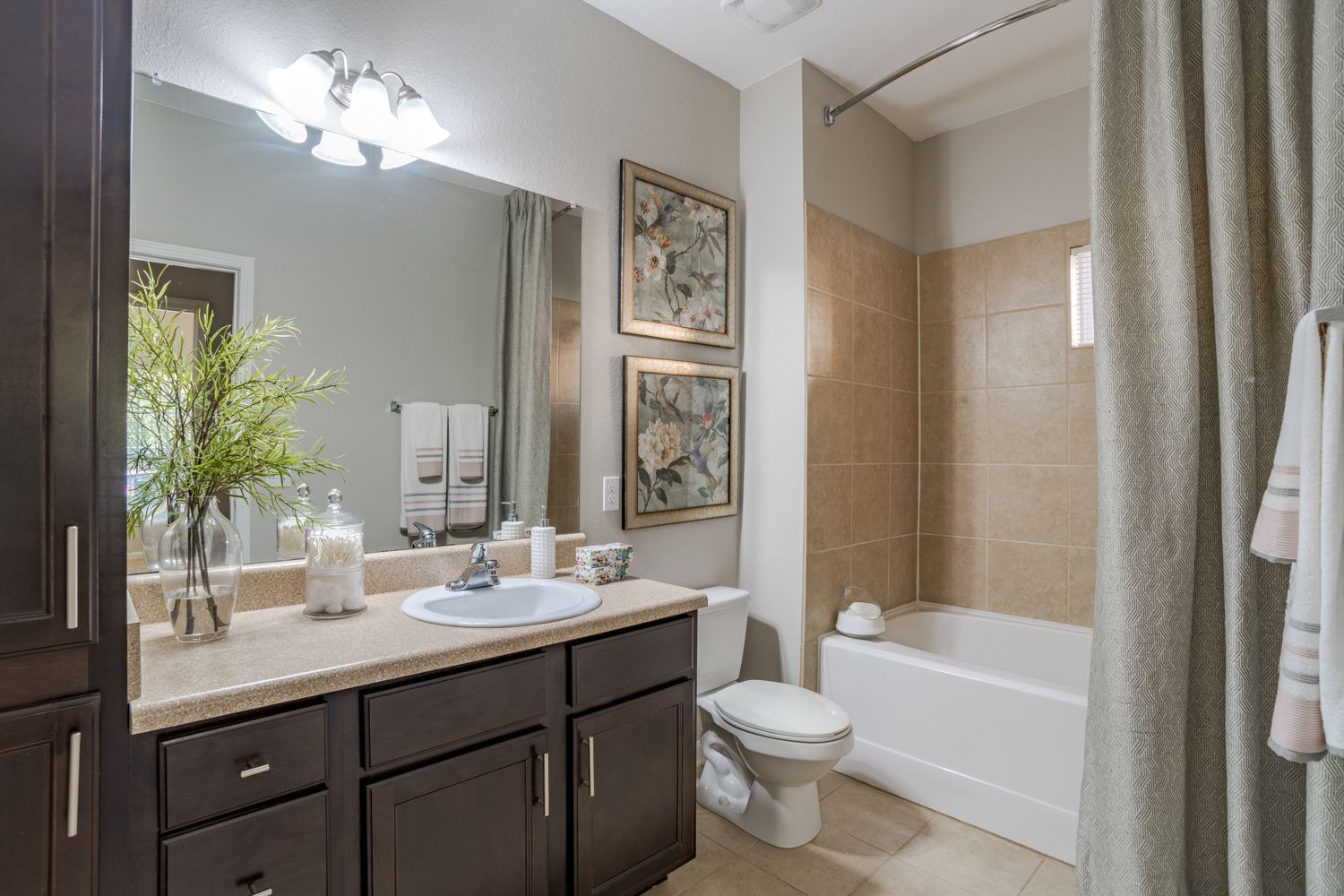 Bathroom with dark brown vanity, white sink, beige tile, and shower curtain.