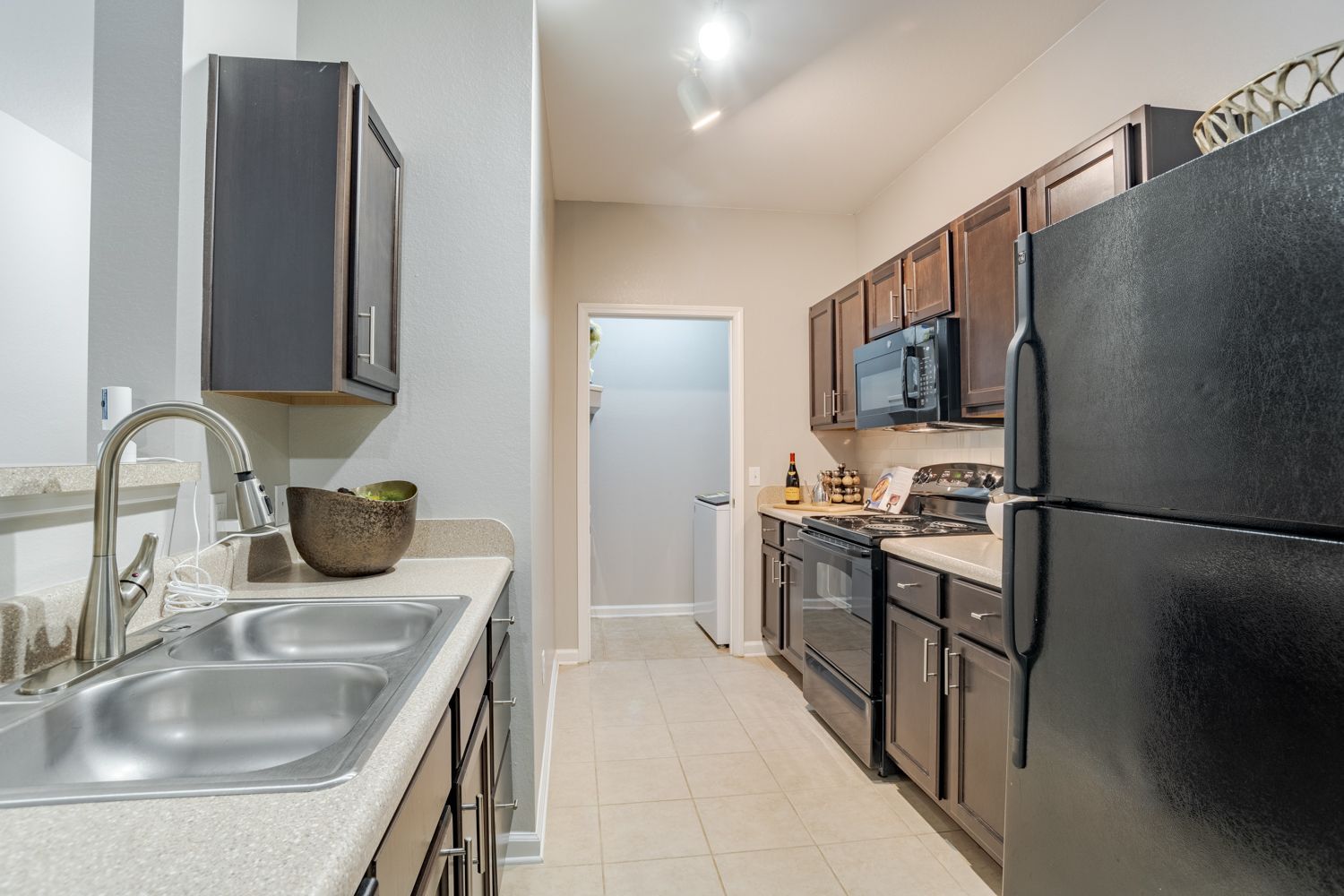 Kitchen with gray cabinets, black appliances, stainless steel sink, and light-colored tile.