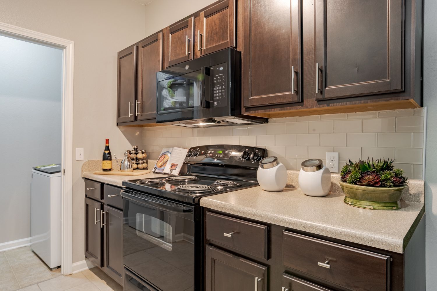 Kitchen with dark brown cabinets, black appliances, and off-white countertops.