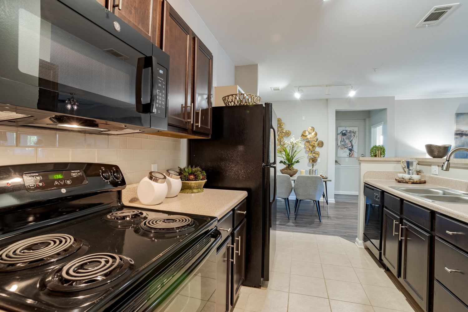 Kitchen with black appliances and dark cabinets, leading to a dining area.