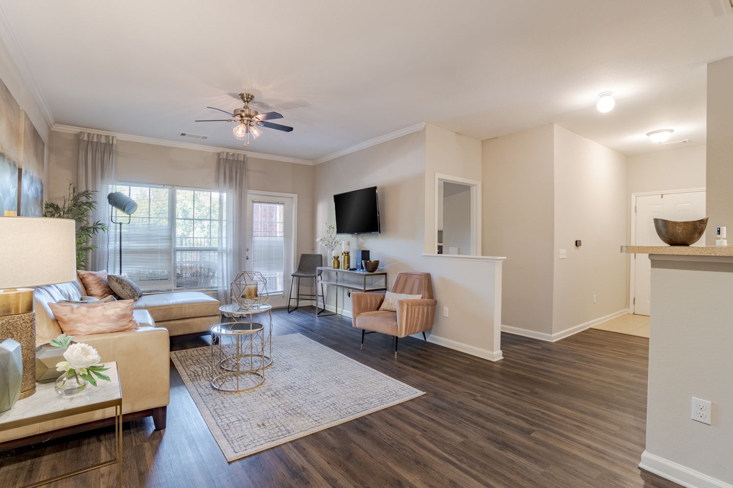 Cozy living room with tan sectional, rug, TV, and pink armchair, and dark wood floors.
