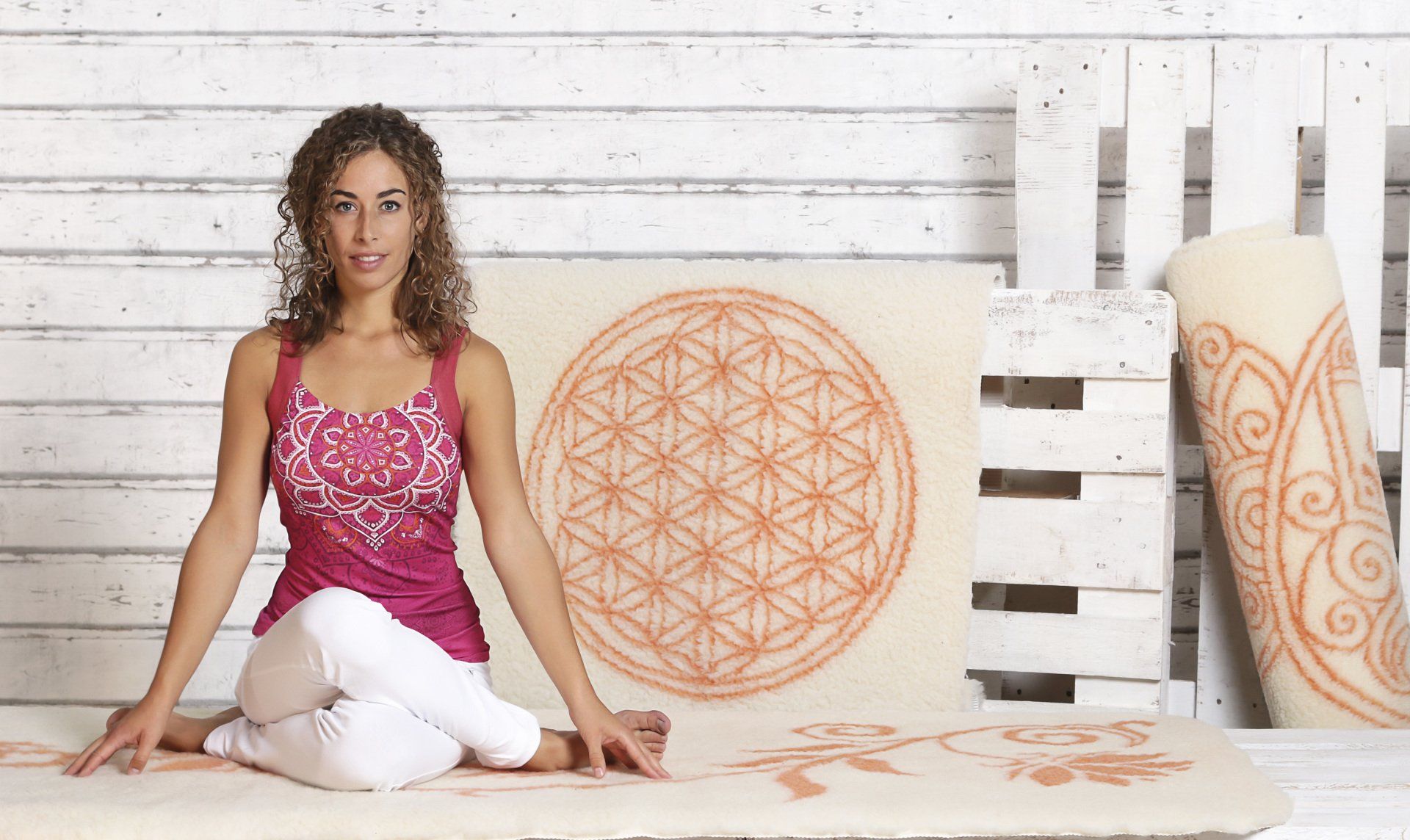 Eine Frau sitzt auf einer Yogamatte mit einer Blume des Lebens darauf.