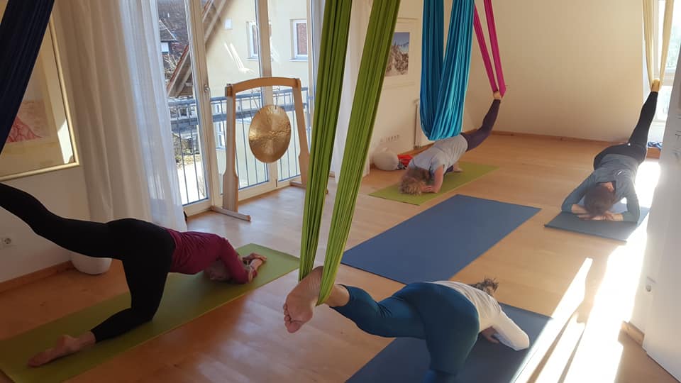 Eine Gruppe von Menschen macht Aerial Yoga in einem Raum