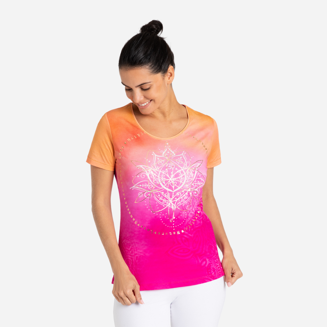 Eine Frau trägt ein rosa-orangefarbenes T-Shirt und eine weiße Hose.
