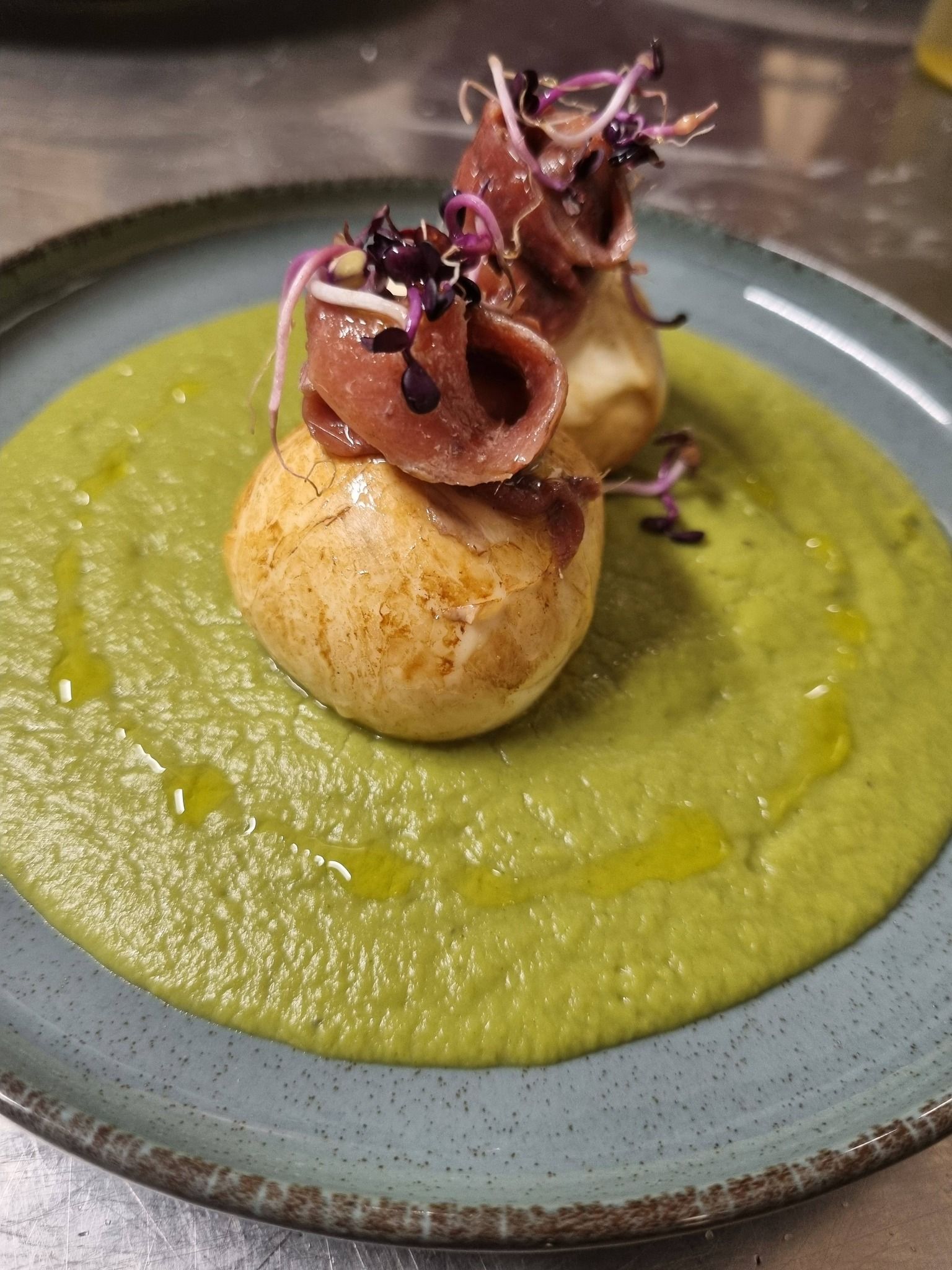 Interno del bar con sedute in pelle nera, tavoli rotondi, mobili in legno e grandi piante.