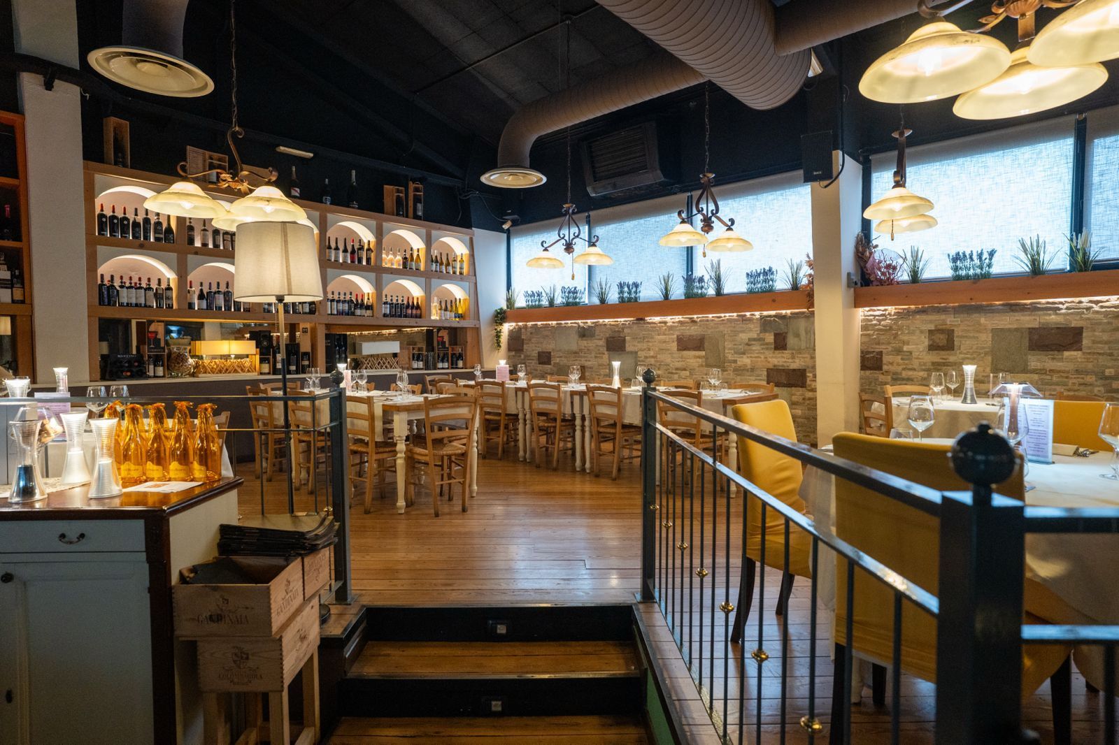 Interno del bar con tavoli e sedie in legno, ampia finestra con vista sul verde esterno.