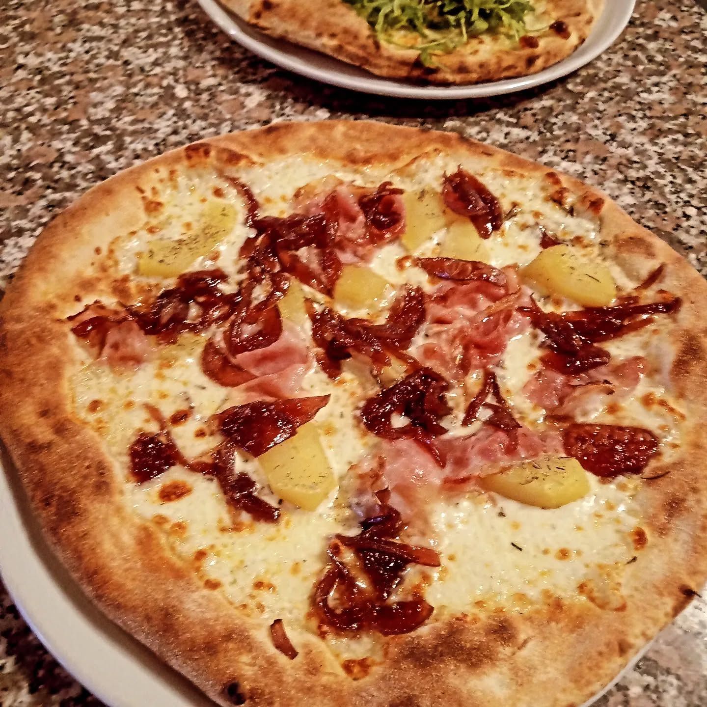 Interno del bar con sedute in pelle nera, tavoli rotondi, mobili in legno e grandi piante.