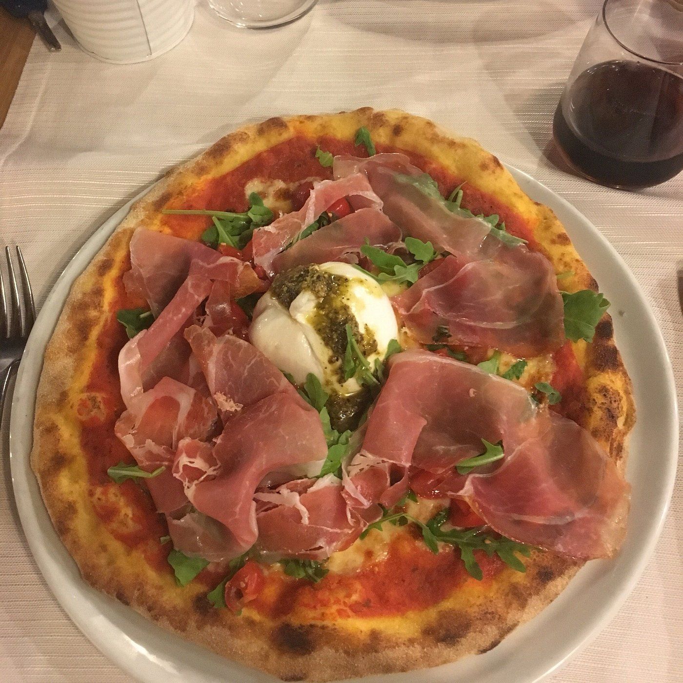 Bar all'aperto con tavoli, sedie e vetrate. Alberi in primo piano, luci e ombre.