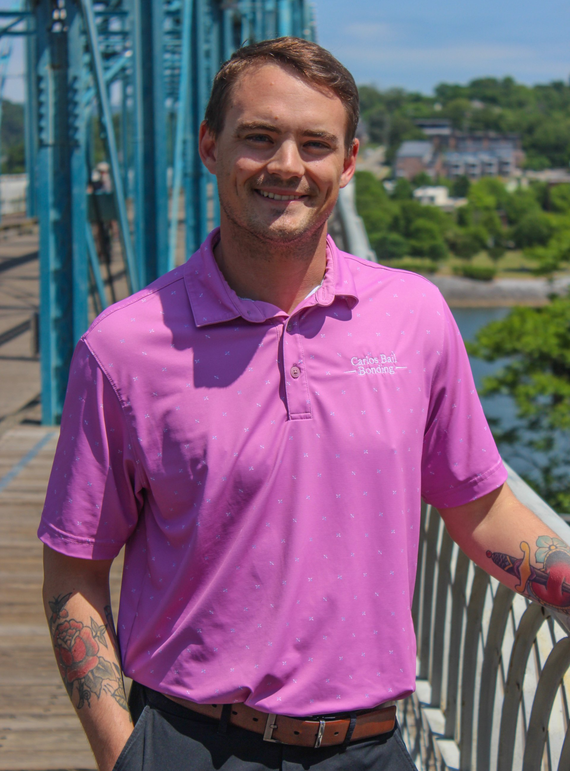 Tanner in a purple polo shirt is standing on a bridge.