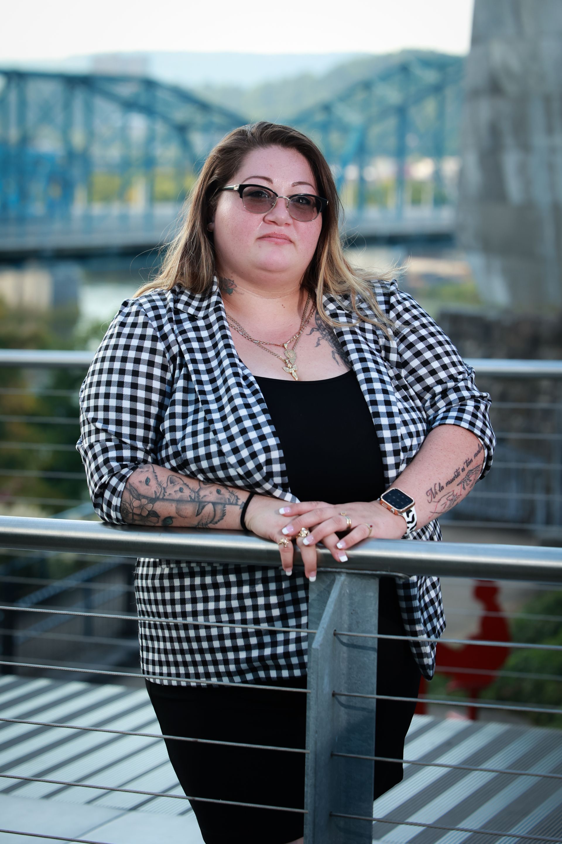 Dakota wearing sunglasses and a plaid shirt is leaning on a railing.