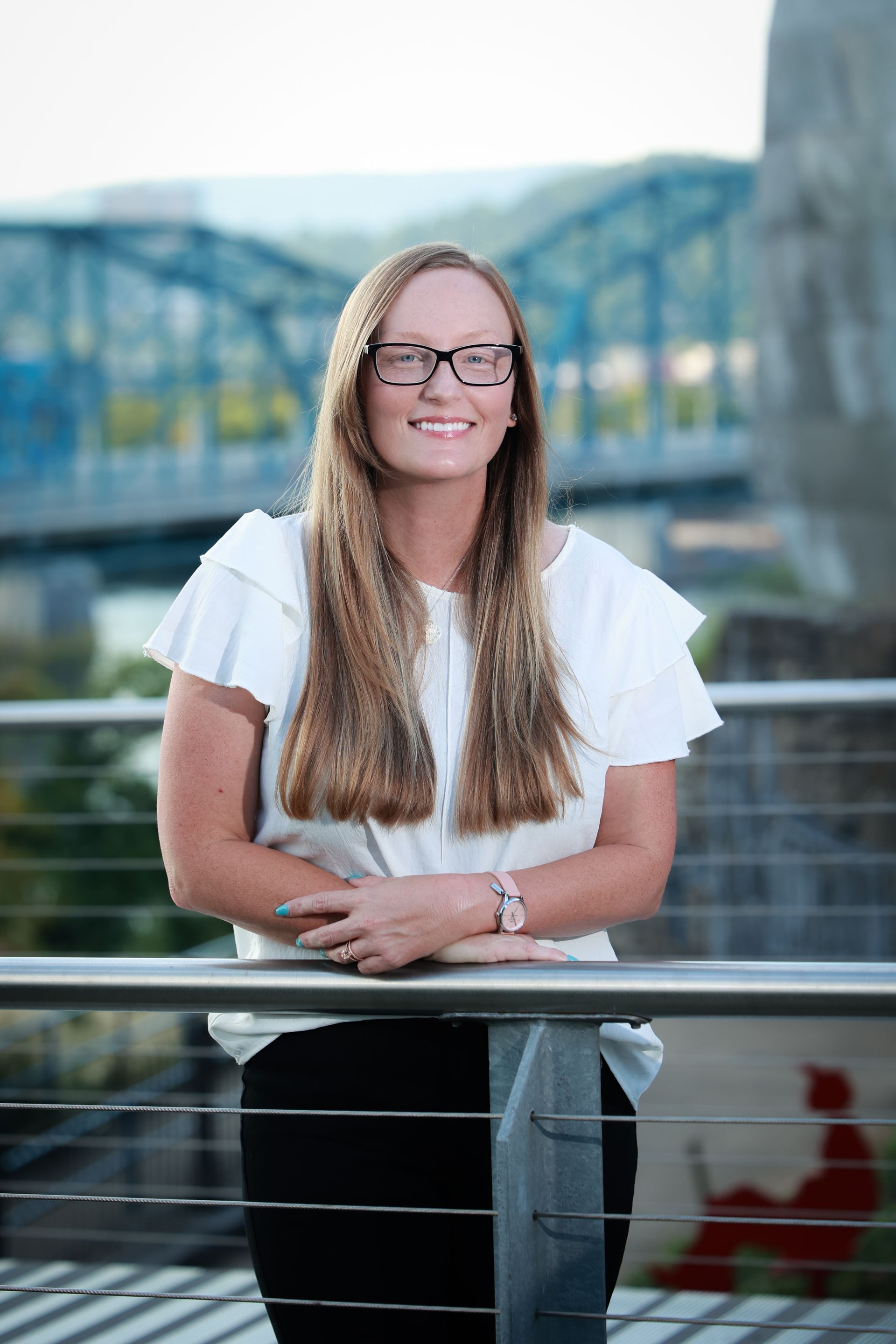 Tammy wearing glasses and a white shirt is standing next to a railing.