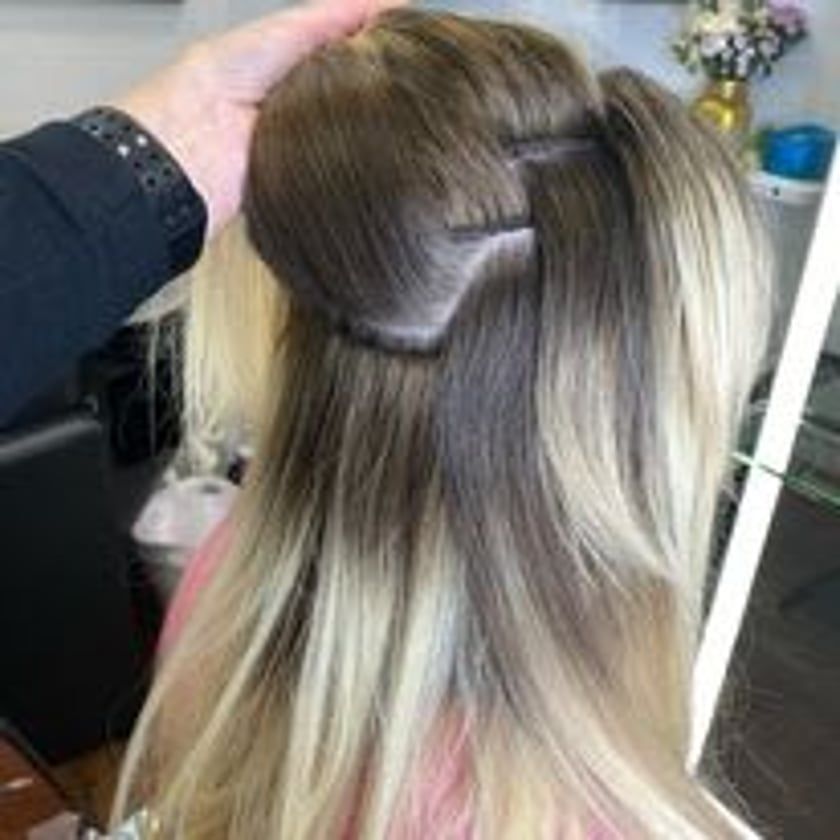 Blonde hair styled, with dark roots, and folded up in sections. A hand holds the hair in the upper left.