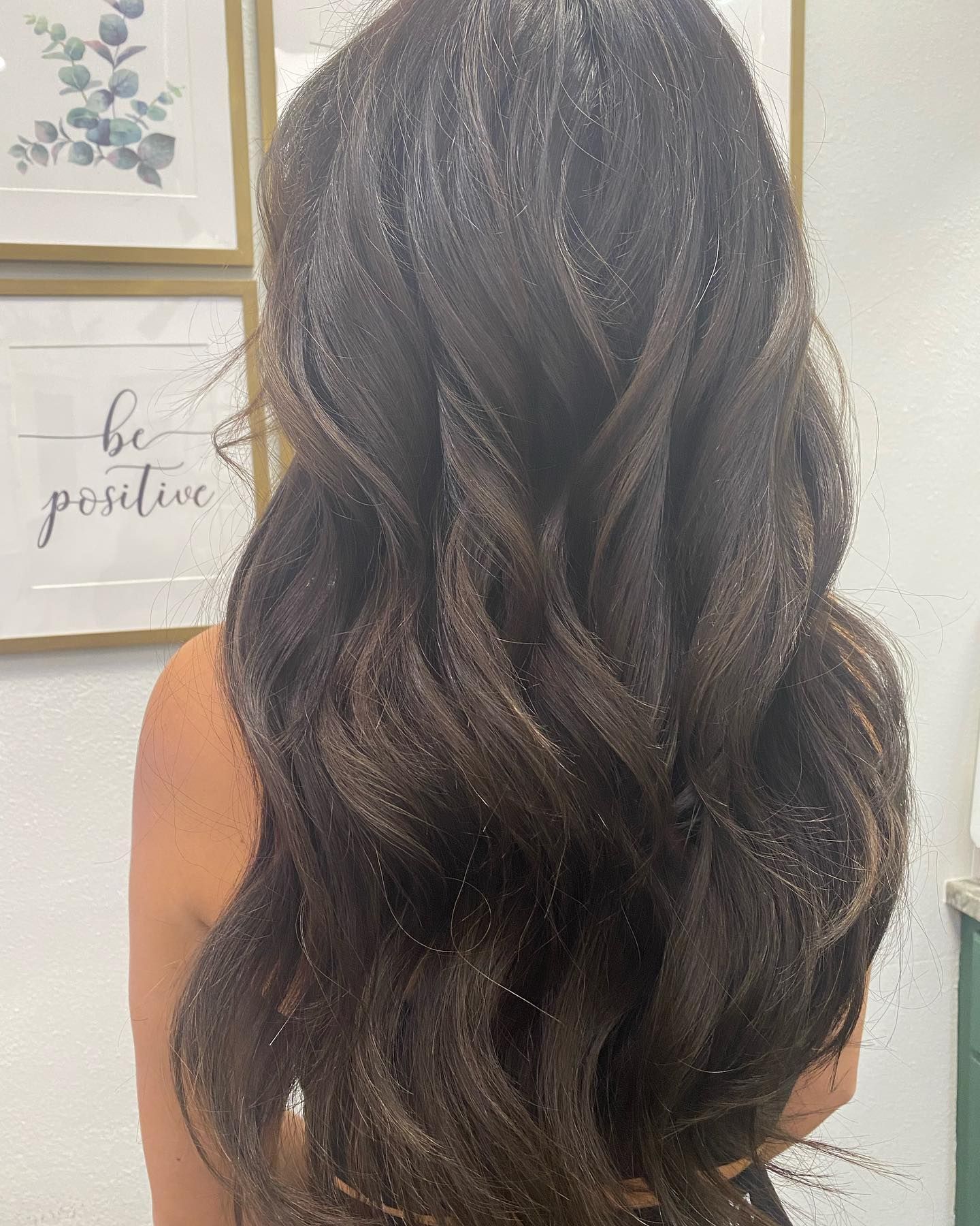 Long, dark wavy hair, possibly styled, with visible glitter; partially framed by wall art.