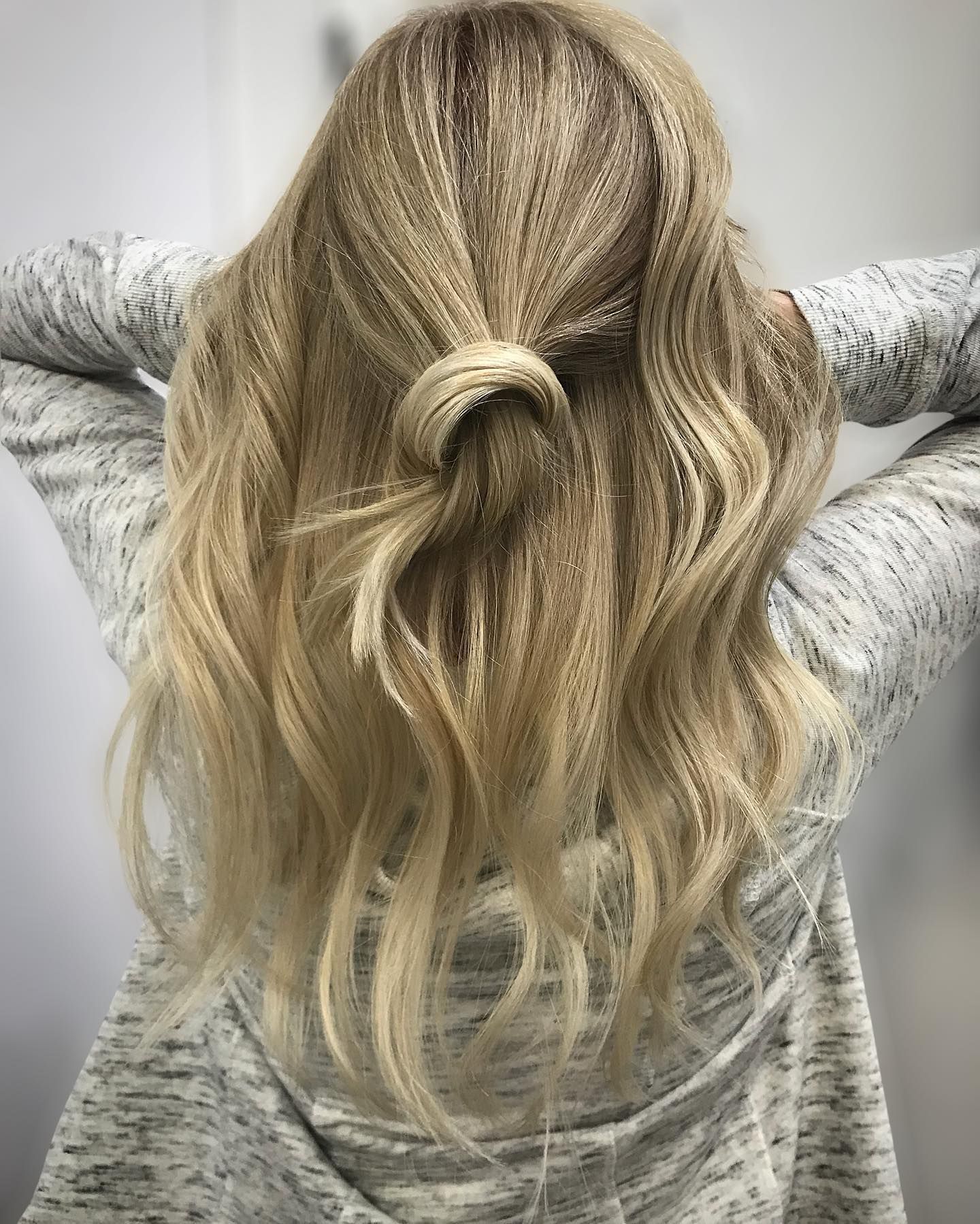 Blonde hair styled in a half-up knot, with loose waves. The person is wearing a gray hoodie.