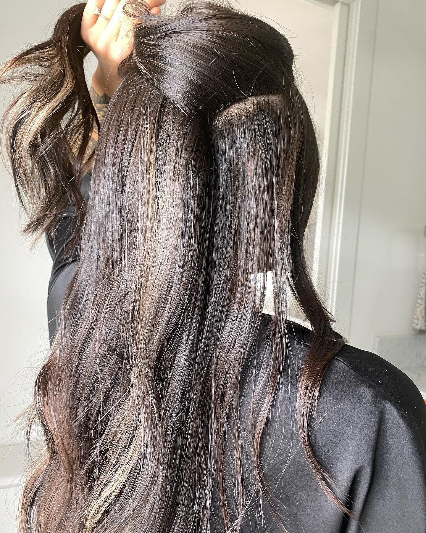 Woman with dark, wavy hair, holding a section up, in a bright setting.