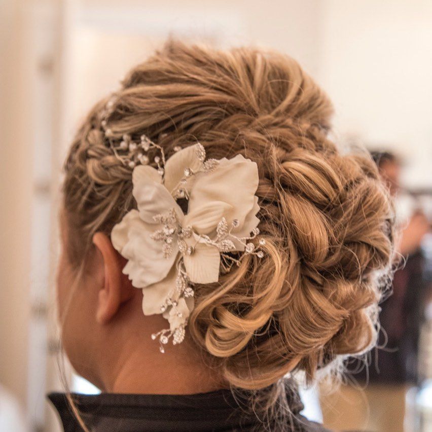 Woman with blonde updo hairstyle, adorned with a large white flower and crystal accents.