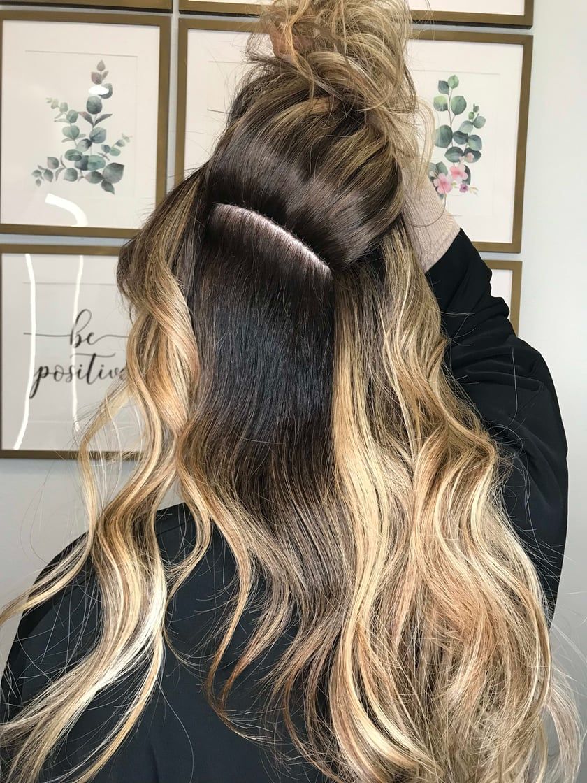 Woman with blonde wavy hair, partially up, dark roots visible, hair extension seam.