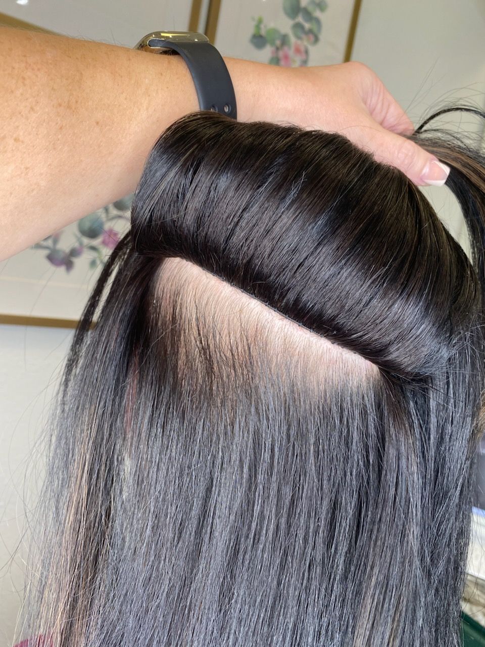 Hair stylist working on a client's black hair, revealing sections and ear.