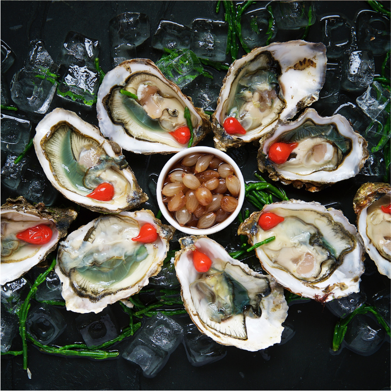 Open oesters op ijs met zeekraal, een schaal met uitjes in het midden en pepertjes in de oester.