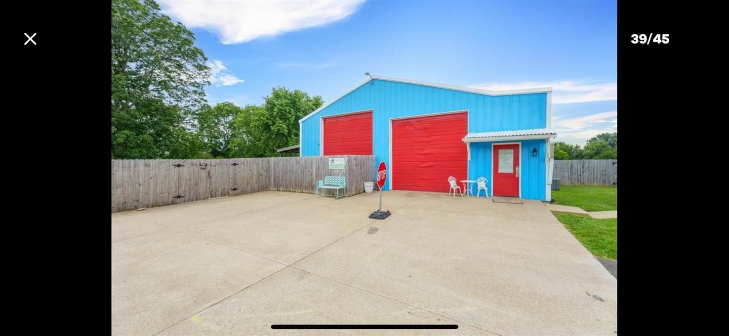A blue garage with red doors and a red door. Concrete patio with a basketball hoop and wooden fence.