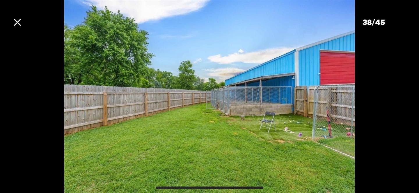 Green grass and a wooden fence border the yard of a blue and red building under a blue sky.