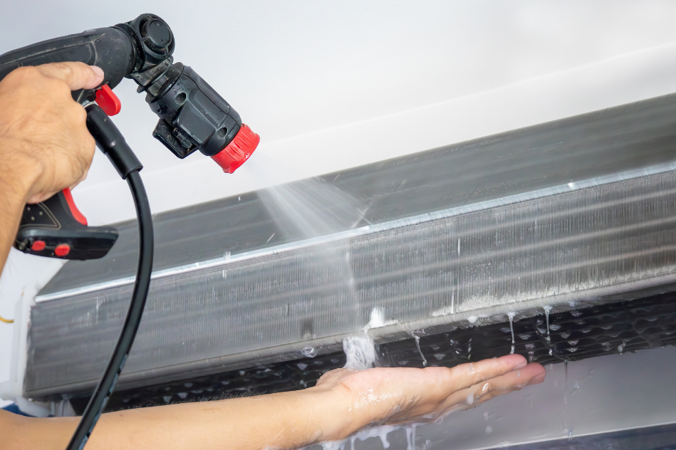 A person is cleaning an air conditioner with a spray bottle.