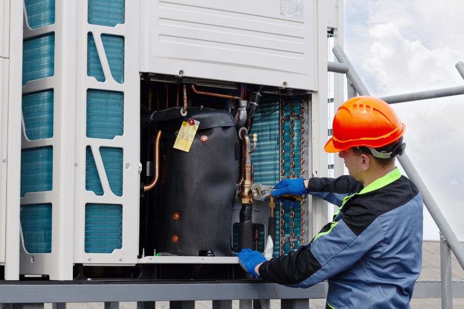 A man wearing a hard hat is working on an air conditioner.