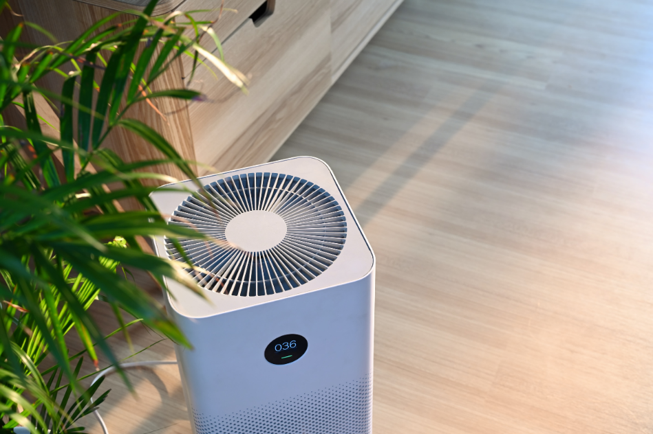 A white air purifier is sitting on a wooden floor next to a plant.