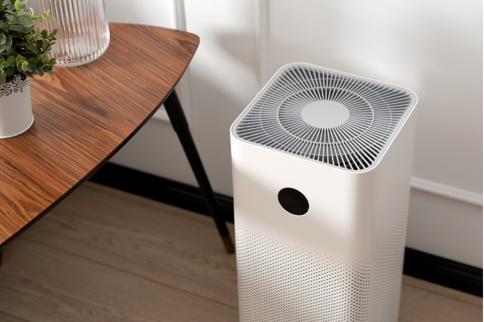 A white air purifier is sitting on the floor next to a wooden table.