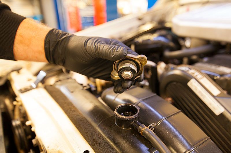 A Person Is Holding a Radiator Cap Over a Car Engine — Lismore Car Repairs in Lismore, NSW