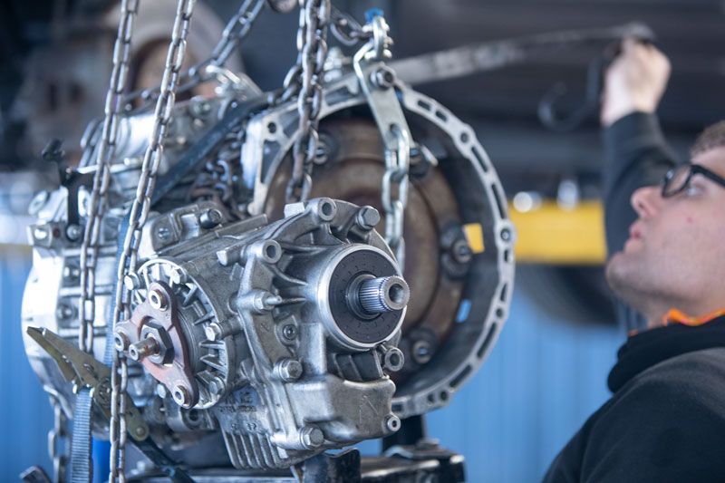 A Man Is Working on A Car Engine with Chains Hanging from It — Lismore Car Repairs in Lismore, NSW