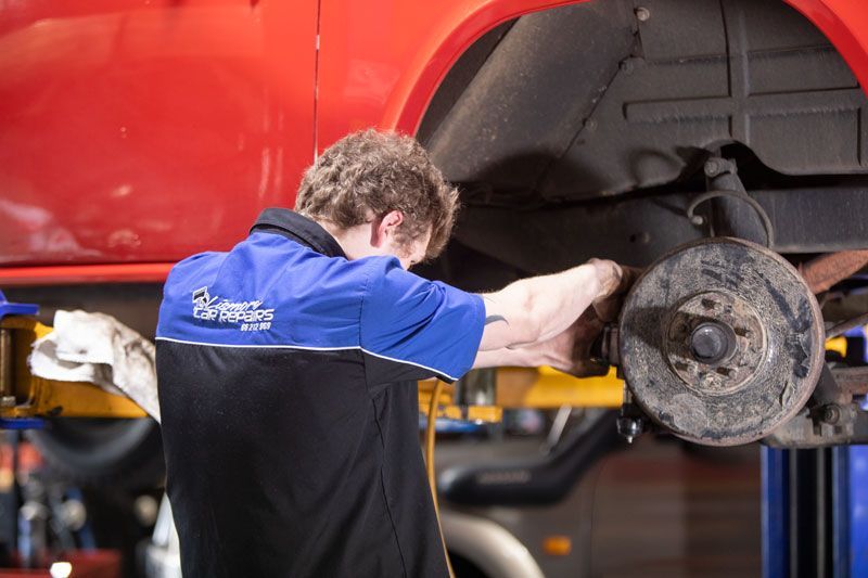 A Man in A Blue Shirt Is Working on A Red Car on A Lift — Lismore Car Repairs in Lismore, NSW