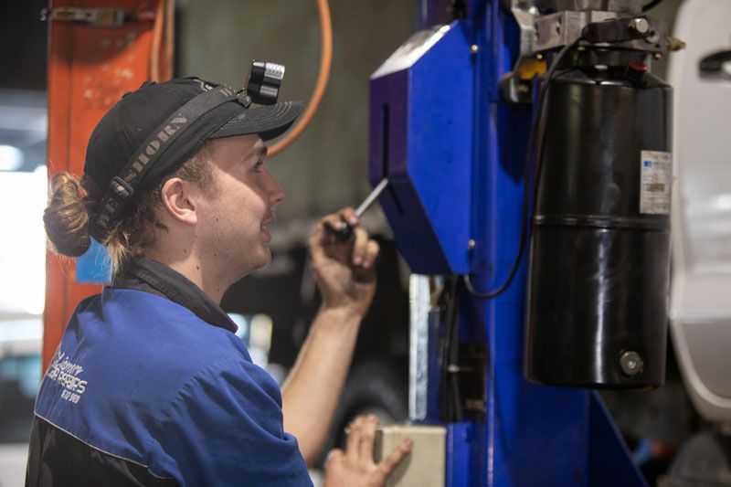 A Man Is Working on A Machine with A Screwdriver in A Garage — Lismore Car Repairs in Lismore, NSW