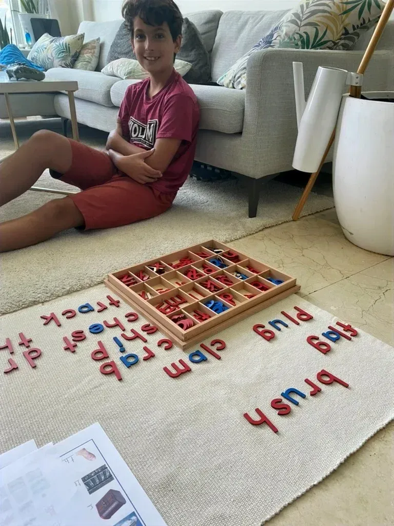 A young boy is sitting on the floor in a living room playing with letters.