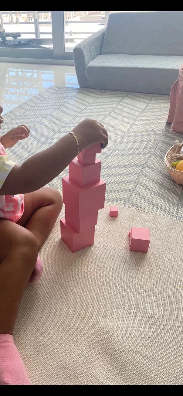 A little girl is sitting on the floor playing with pink blocks.