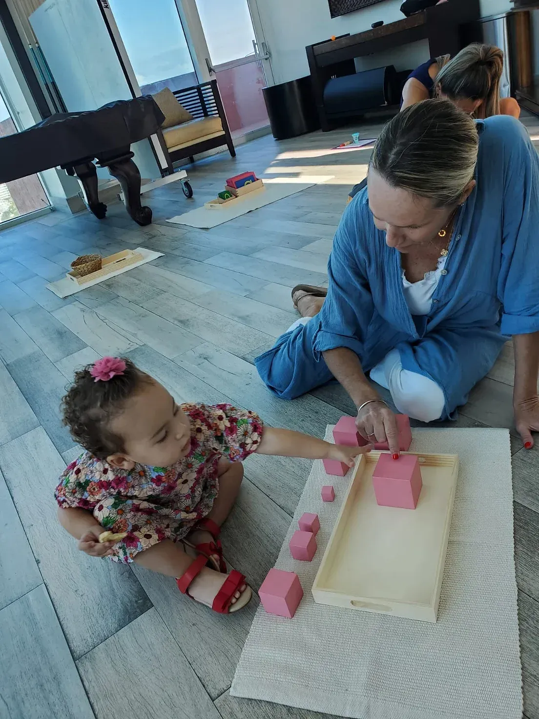 A woman and a little girl are playing with pink blocks on the floor.