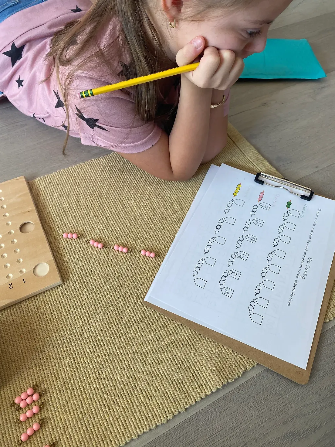 A little girl is laying on the floor writing on a piece of paper with a pencil.