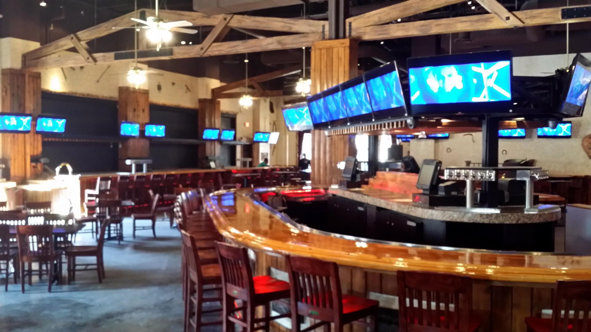 A restaurant with a long bar and a lot of televisions hanging from the ceiling.