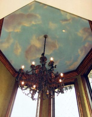 A chandelier is hanging from a ceiling with clouds painted on it