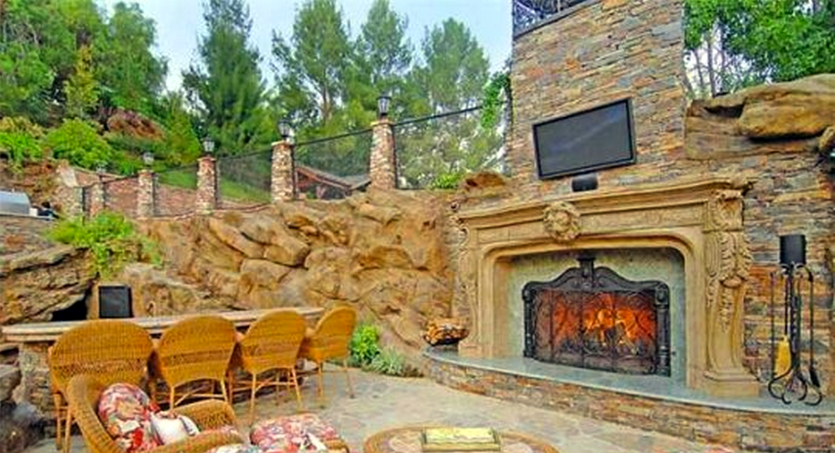 There is a fireplace in the backyard with a television above it.