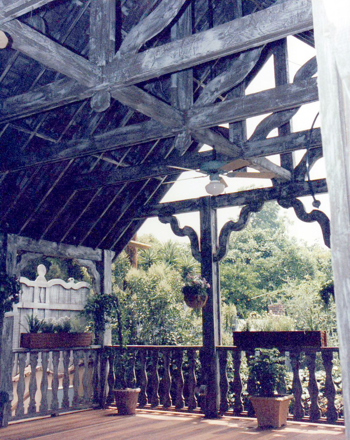 A wooden porch with a ceiling fan and potted plants