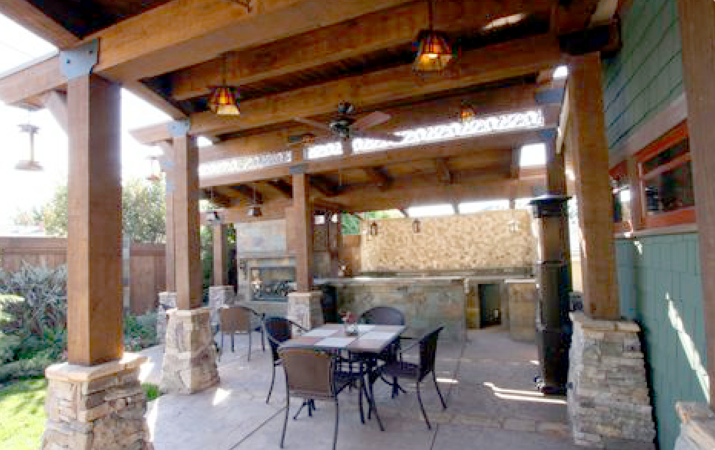 A patio with a table and chairs under a wooden roof.